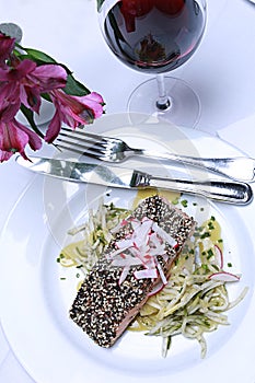 Salmon dish on white tablecloth with glass of red wine