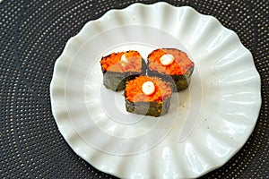 Salmon eggs or Ikura in Japanese style sushi fresh from raw salmon fish served on a white plate on dark background