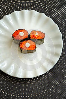 Salmon eggs or Ikura in Japanese style sushi fresh from raw salmon fish served on a white plate on dark background