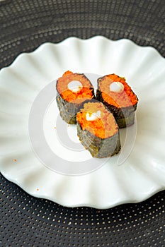 Salmon eggs or Ikura in Japanese style sushi fresh from raw salmon fish served on a white plate on dark background