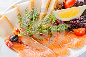 Salmon fillet pieces, sturgeon pieces served with lemon, black olives, herbs, cherry tomato and pomegranate seeds on white plate c