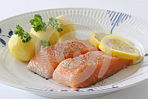 Salmon fillet with potatoes, lemon slices and parsley served on a plate. Close up