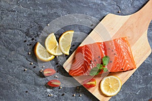 Salmon. Fresh raw salmon fish. Raw salmon fillet with pepper, herbs, lemon, tomato ingredients for cooking on black stone table