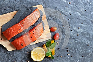 Salmon. Fresh raw salmon fish. Raw salmon fillet with pepper, herbs, lemon, tomato ingredients for cooking on black stone table