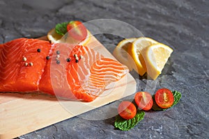 Salmon. Fresh raw salmon fish. Raw salmon fillet with pepper, herbs, lemon, tomato ingredients for cooking on black stone table