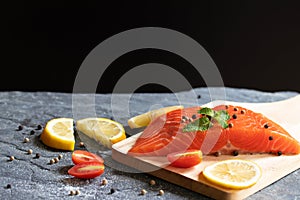 Salmon. Fresh raw salmon fish. Raw salmon fillet with pepper, herbs, lemon, tomato ingredients for cooking on black stone table