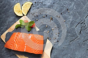 Salmon. Fresh raw salmon fish. Raw salmon fillet with pepper, herbs, lemon, tomato ingredients for cooking on black stone table