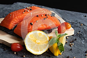 Salmon. Fresh raw salmon fish. Raw salmon fillet with pepper, herbs, lemon, tomato ingredients for cooking on black stone table