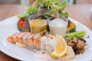 Salmon grilled with cream sauces, lemon, and colorful vegetable on a white plate.