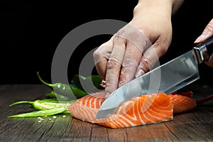 Salmon is in the hands of the Japanese chef and meticulously done, He is using a knife to slice salmon fillet for sashimi and sush
