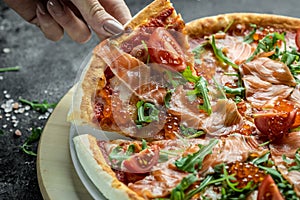 Salmon Italian Pizza with red caviar, tomatoes and aragula ready to eat on a dark background. banner, menu, recipe place for text