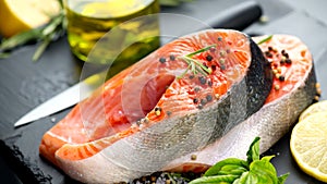 Salmon. Raw trout fish steak with herbs and lemon on black slate background. Cooking