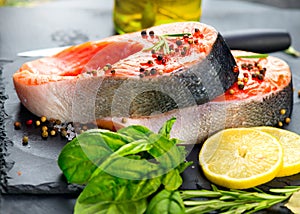 Salmon. Raw trout fish steak with herbs and lemon on black slate background. Cooking