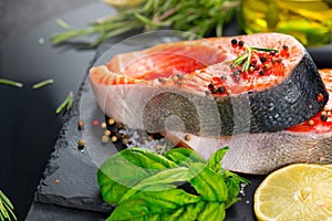 Salmon. Raw trout fish steak with herbs and lemon on black slate background. Cooking