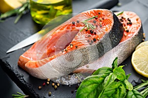 Salmon. Raw trout fish steak with herbs and lemon on black slate background. Cooking, seafood