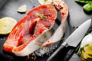 Salmon. Raw trout fish steak with herbs and lemon on black slate background. Cooking, seafood