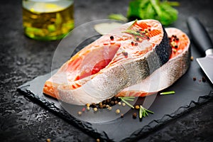 Salmon. Raw trout fish steak with herbs and lemon on black slate background. Cooking, seafood