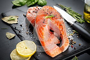 Salmon. Raw trout fish steak with herbs and lemon on black slate background. Cooking, seafood. Healthy eating