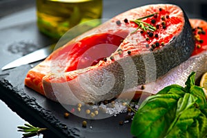 Salmon. Raw trout fish steak with herbs and lemon on black slate background. Cooking, seafood. Healthy eating