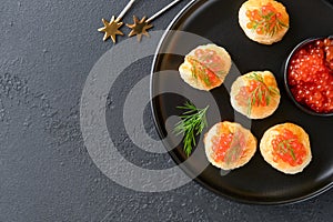 Salmon red caviar toast. Christmas canape or toast with red caviar on black plate on dark background. Idea to xmas snack
