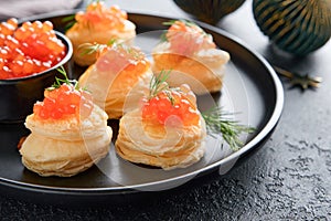 Salmon red caviar toast. Christmas canape or toast with red caviar on black plate on dark background. Idea to xmas snack