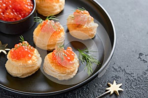 Salmon red caviar toast. Christmas canape or toast with red caviar on black plate on dark background. Idea to xmas snack. Gourmet