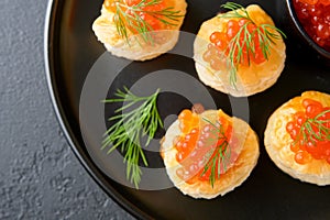 Salmon red caviar toast. Christmas canape or toast with red caviar on black plate on dark background. Idea to xmas snack. Gourmet