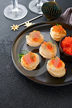 Salmon red caviar toast. Christmas canape or toast with red caviar on black plate on dark background. Idea to xmas snack. Gourmet