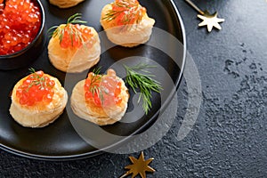 Salmon red caviar toast. Christmas canape or toast with red caviar on black plate on dark background. Idea to xmas snack. Gourmet