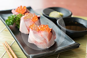 Salmon Roe on Hamachi sushi on black plate along with Japanese s