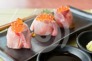 Salmon Roe on Hamachi sushi on black plate along with Japanese sauce and green leaf decoration, Japanese food, close up at sushi