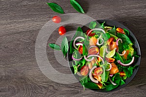 Salmon salad, Top view from above fresh tomato, onion with spinach, lettuce and basil in black bowl on dark background.