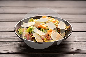 Salmon salad with vegetables and lattice salad served on a black plate on a light table. Mediterranean restaurant diet