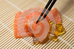 Salmon Sashimi mixed with Fish oil capsules with chopstick grab