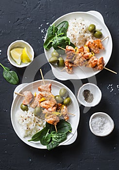 Salmon skewers, olives, spinach, rice - healthy lunch table. Grilled salmon fish skewer and side dish on a dark background