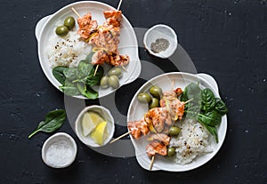 Salmon skewers, olives, spinach, rice - healthy lunch table. Grilled salmon fish skewer and side dish on a dark background