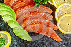 Salmon sliced with lemon and avocado on marble plate