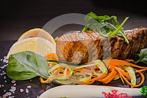 Salmon steak with lemon greens and sauce on stone with salt