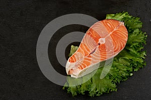 Salmon steak raw fish with a lemon prepared for cooking. Top view on black slate table.