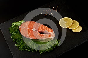 Salmon steak raw fish with a lemon prepared for cooking. Top view on black slate table.