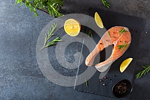 Salmon steak raw fish prepared for cooking. Fresh trout steak with salt, pepper, lemon and rosemary on black slate board on dark