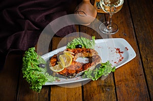 Salmon steak on a white plate with lemon, olives and lettuce. On an old wooden background.