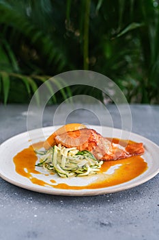 Salmon steak with zucchini noodles with orange sauce and orange on a white plate