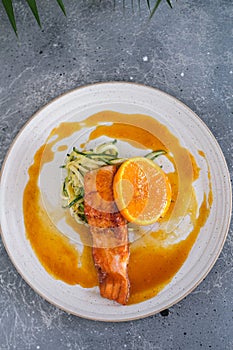 Salmon steak with zucchini noodles with orange sauce and orange on a white plate