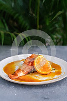 Salmon steak with zucchini noodles with orange sauce and orange on a white plate