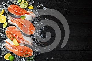 Salmon steaks on ice on black wooden table top view. Fish food concept. Copy space
