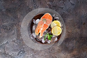 Salmon steaks on ice withlemon slice on wooden plate