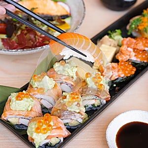 Salmon sushi. A hand using chopsticks to hold a salmon sushi, soft focus. Window light