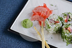 Salmon sushi rolls served on a white plate with ginger and wasabi sauce in a restaurant on table. Japanese cuisine.