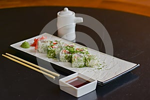 Salmon sushi rolls served on a white plate with ginger and wasabi and soy sauce in a restaurant table. Japanese cuisine.